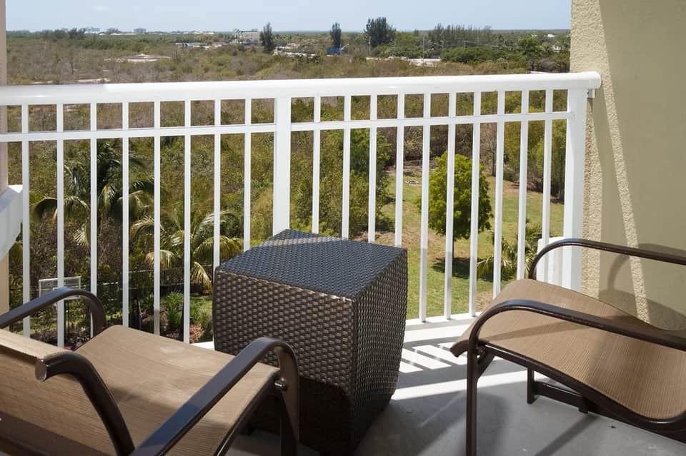 High-rise balcony with white railing, lounge chairs, black side table, and panoramic landscape view