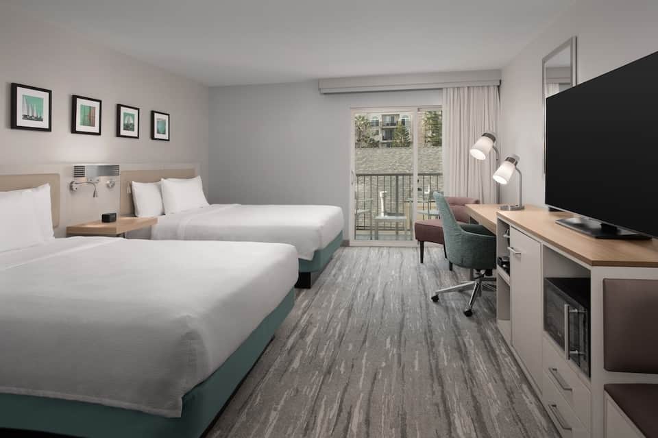 Hotel bedroom with two queen beds, desk area, and glass balcony door