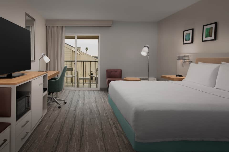 Contemporary hotel room with queen bed, desk, flat-screen TV, balcony, and ocean view