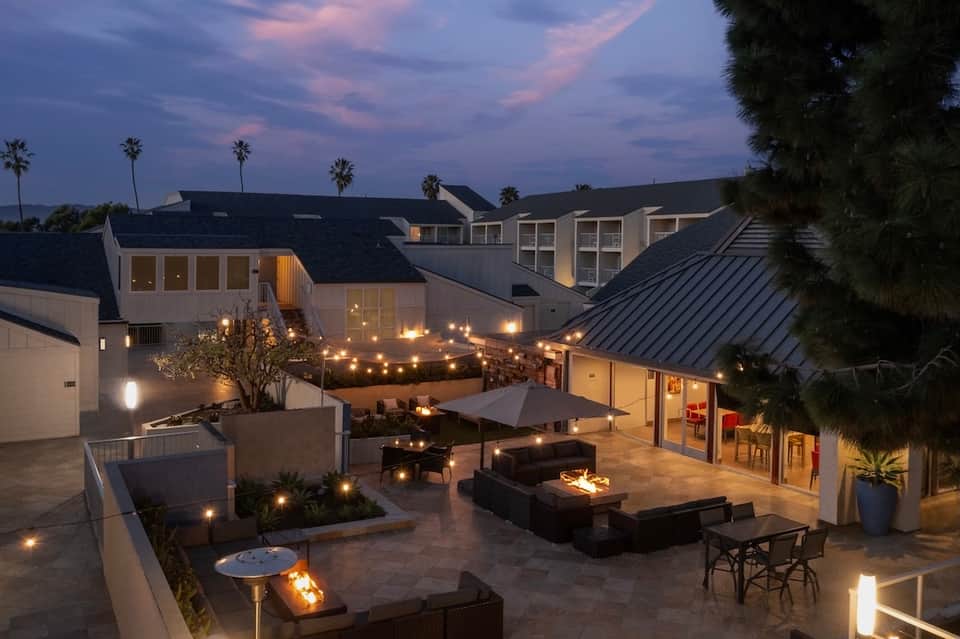 Illuminated resort courtyard at night with fire pits, lounge seating, and modern architecture