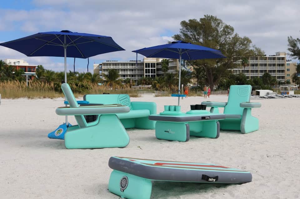 Beach lounge area with turquoise modular seating, blue umbrellas, and ocean-view setting