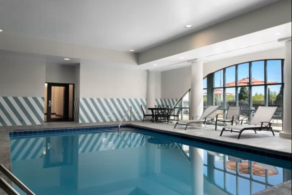 Modern indoor pool with floor-to-ceiling windows, striped wall detail, and adjacent lounge seating area