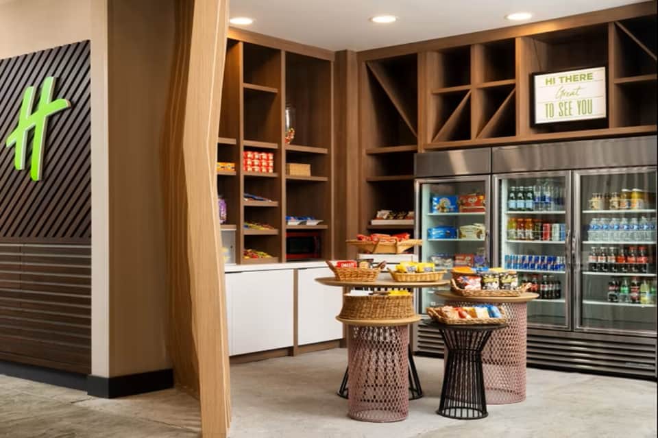 Modern hotel lobby snack bar with wooden shelving, coolers, and grab-and-go items