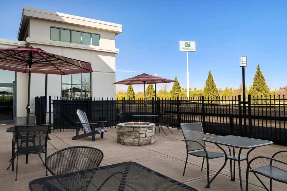 Outdoor patio area with fire pit, umbrellas, metal furniture, and Holiday Inn signage