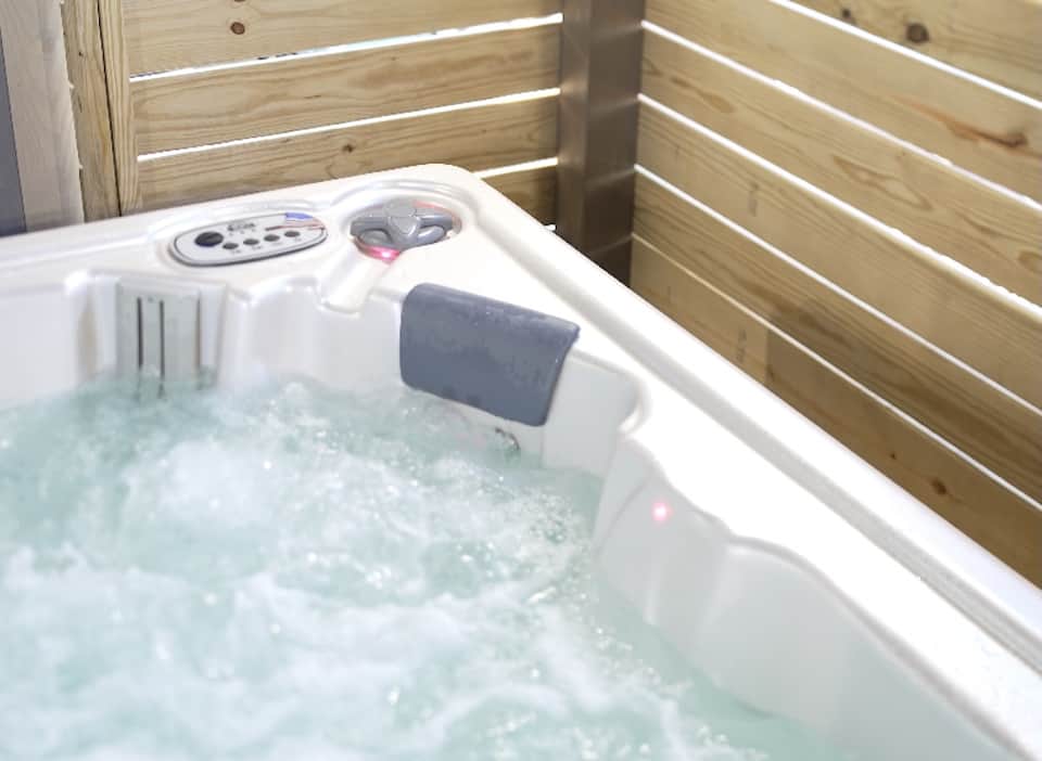 Outdoor hot tub with white jets and controls, surrounded by wooden railings and water features
