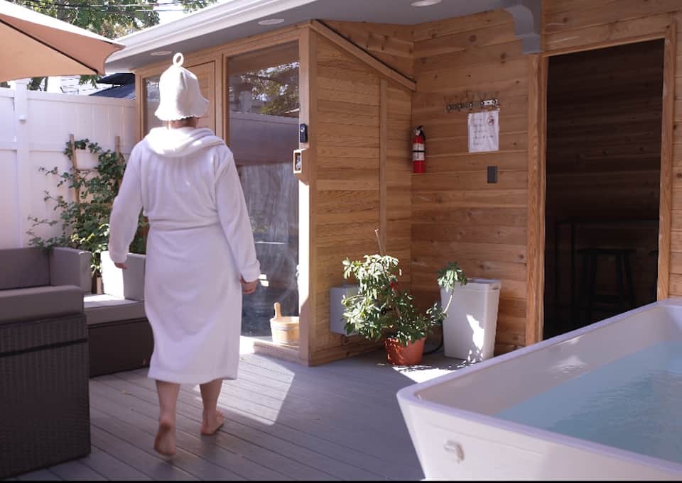 Woman in robe walking toward spa facilities with sauna and hot tub on scenic patio