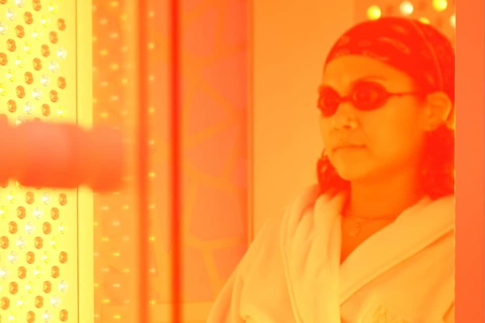 Infrared sauna room with person wearing red cap and orange-tinted heat therapy lighting