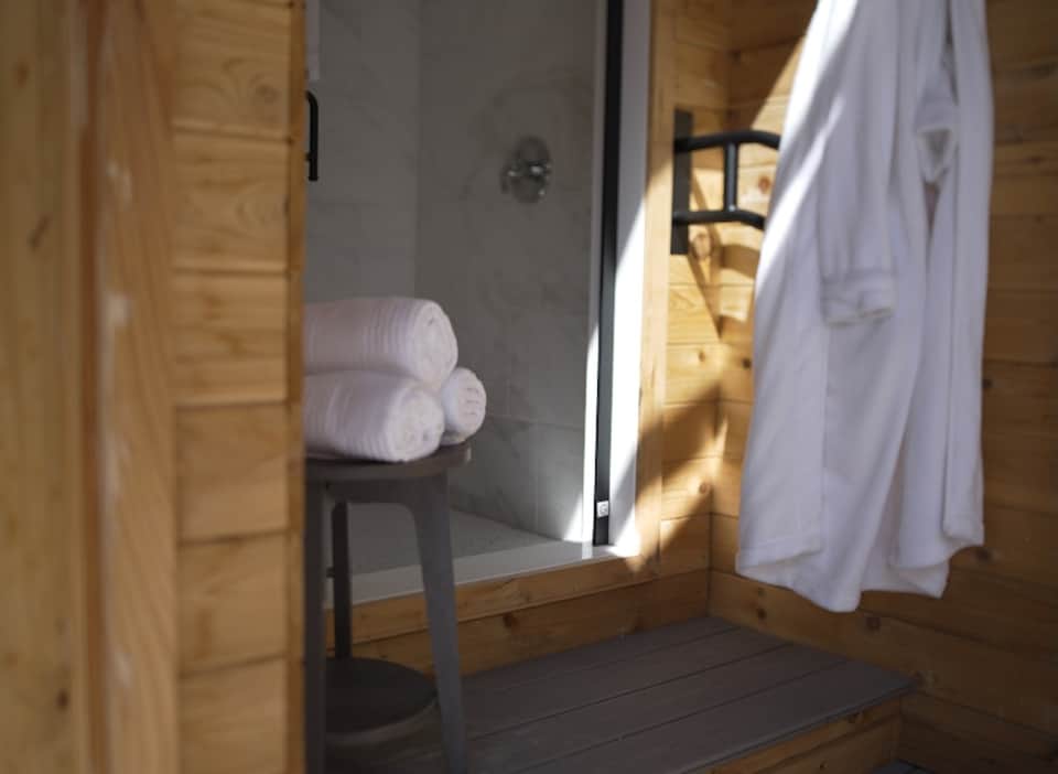 Bathroom entrance showing rolled white towels on shelf, wooden doors, and white spa robes hanging