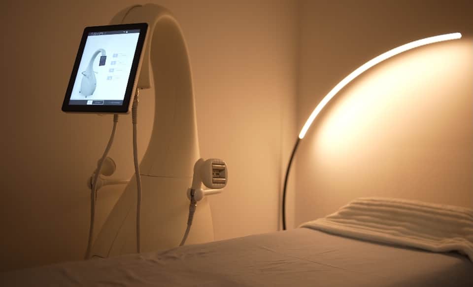 Spa treatment pod with tablet display, neon light, and white pillow in warm-toned wellness room