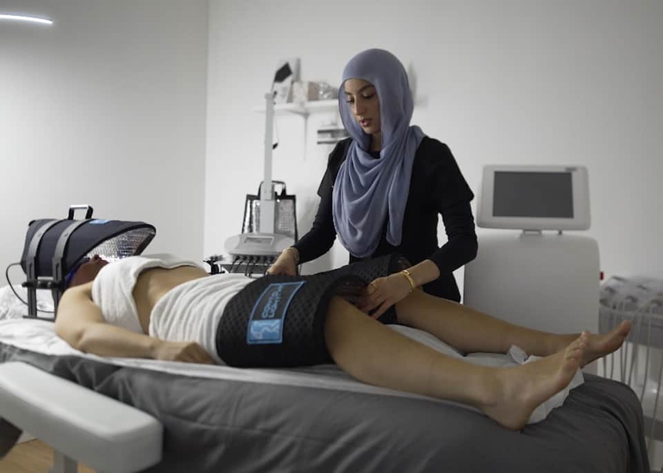 Technician performing electronic massage therapy on client's leg in modern wellness clinic