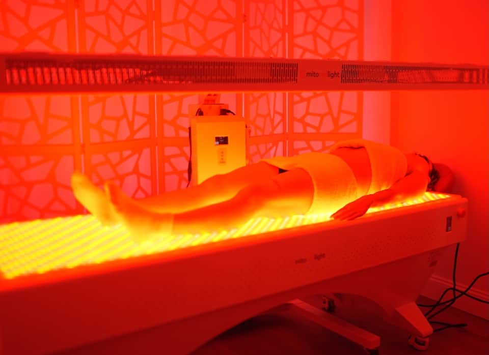 Red and yellow infrared light therapy bed with therapeutic tunnel design for wellness treatments at spa