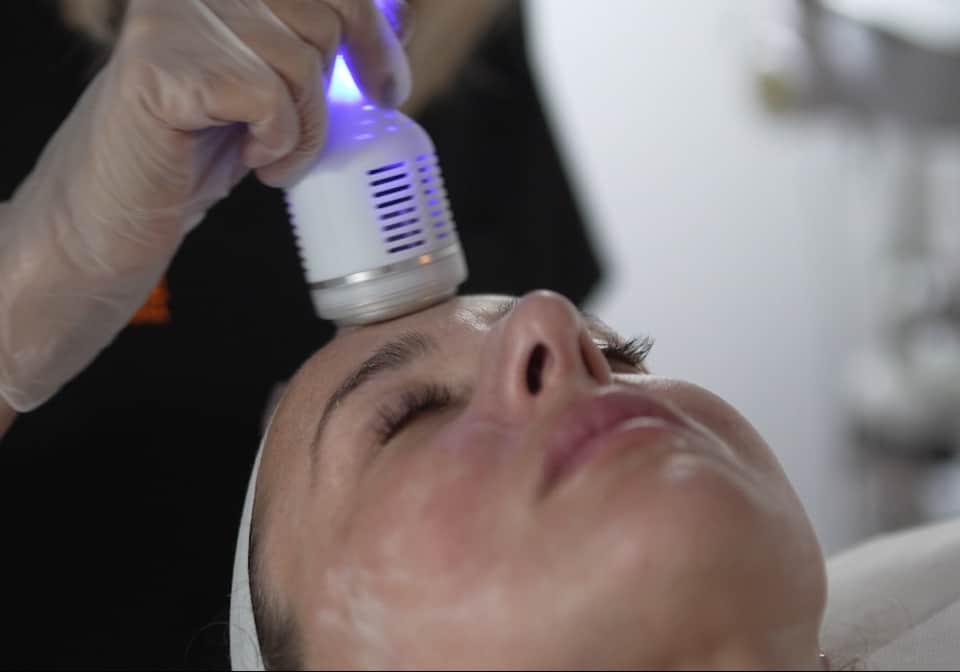 Medical professional performing laser skin treatment on patient's face with blue light technology device