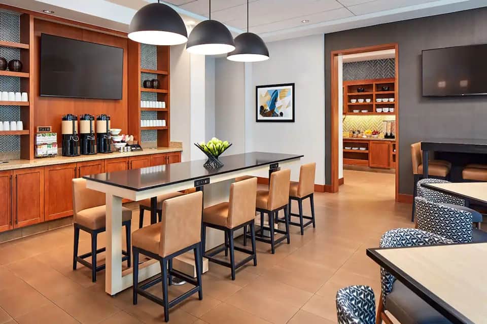 Modern resort lounge with high-top dining table, orange cabinetry, pendant lighting, and fireplace