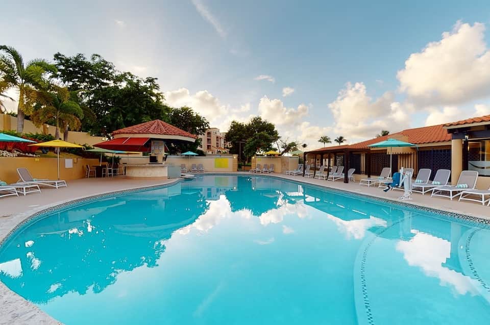 Resort swimming pool with turquoise water, lounge chairs, colorful umbrellas, and tropical landscaping