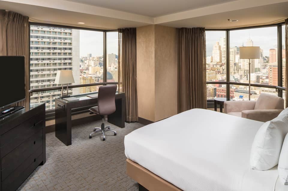 High-rise hotel suite with panoramic city views, work desk, and modern furnishings