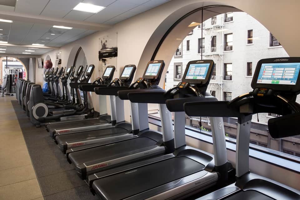Modern fitness center with row of treadmills and exercise equipment along large windows