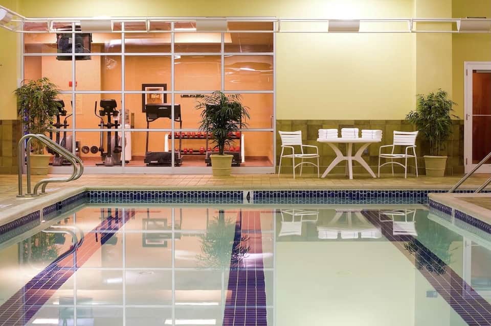Indoor swimming pool facility with lap lanes, gym visible through glass partition wall