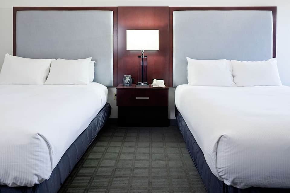 Hotel room with two queen beds, gray headboards, and dark wood nightstands