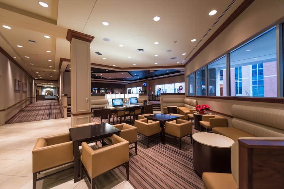 Hotel business center with reception desk, computers, seating areas, and floor-to-ceiling windows