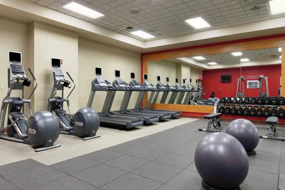 Hotel gym with cardio equipment, exercise balls, weights, and mirrored walls