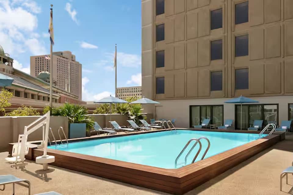Urban hotel rooftop pool with turquoise water, lounge chairs, umbrellas, and city skyline