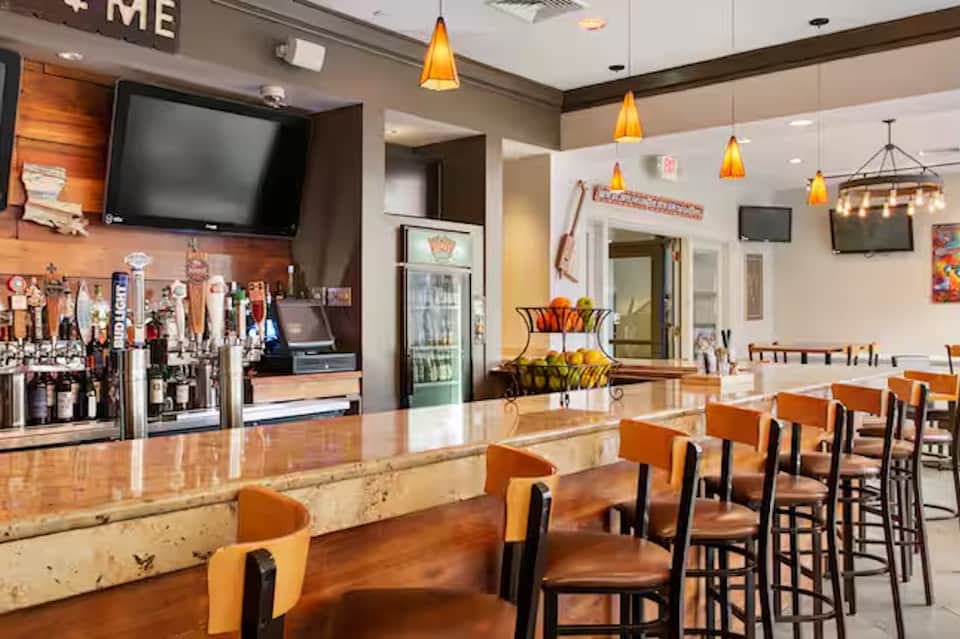 Casual sports bar dining area with orange seating, full bar counter, and pendant lighting