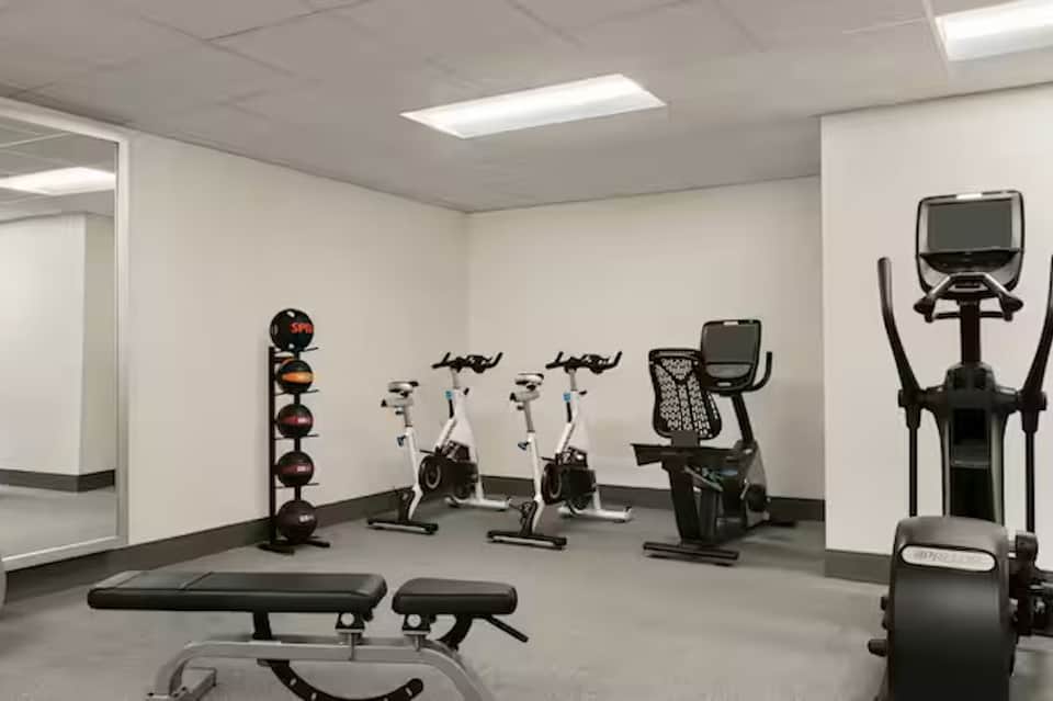 Compact fitness room with exercise bikes, weight rack, bench, and elliptical machine