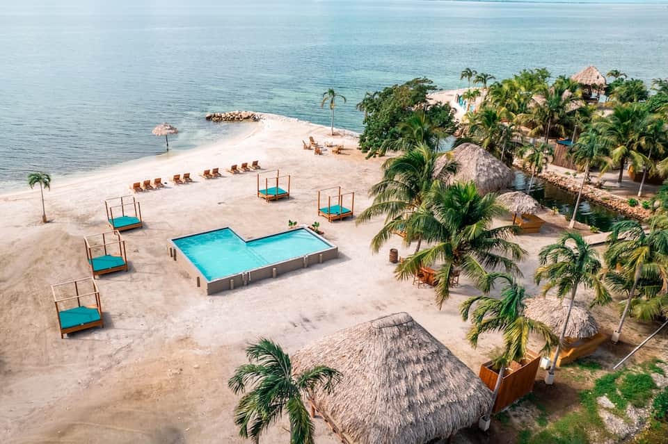 Tropical beach resort with turquoise pools, thatched-roof huts, palm trees, and Caribbean ocean view