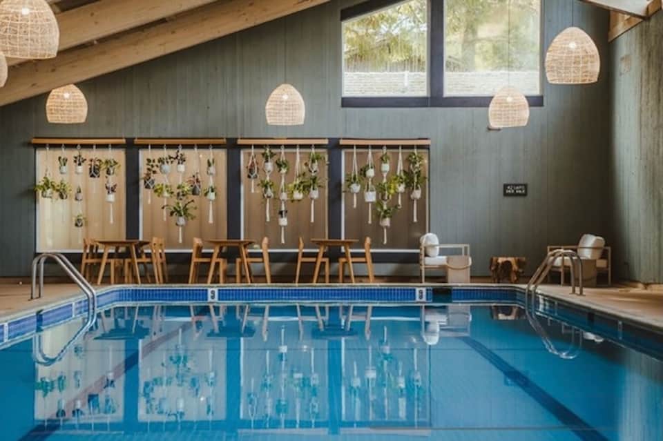 Indoor pool with hanging planters, wooden ceiling beams, and seating area