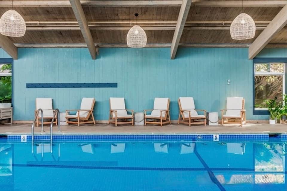 Indoor pool area with light wood ceiling, blue water, and lounge chairs