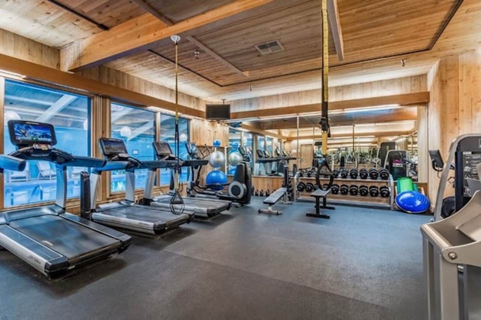 Modern fitness center with treadmills, exercise equipment, wooden ceiling beams, and ocean views