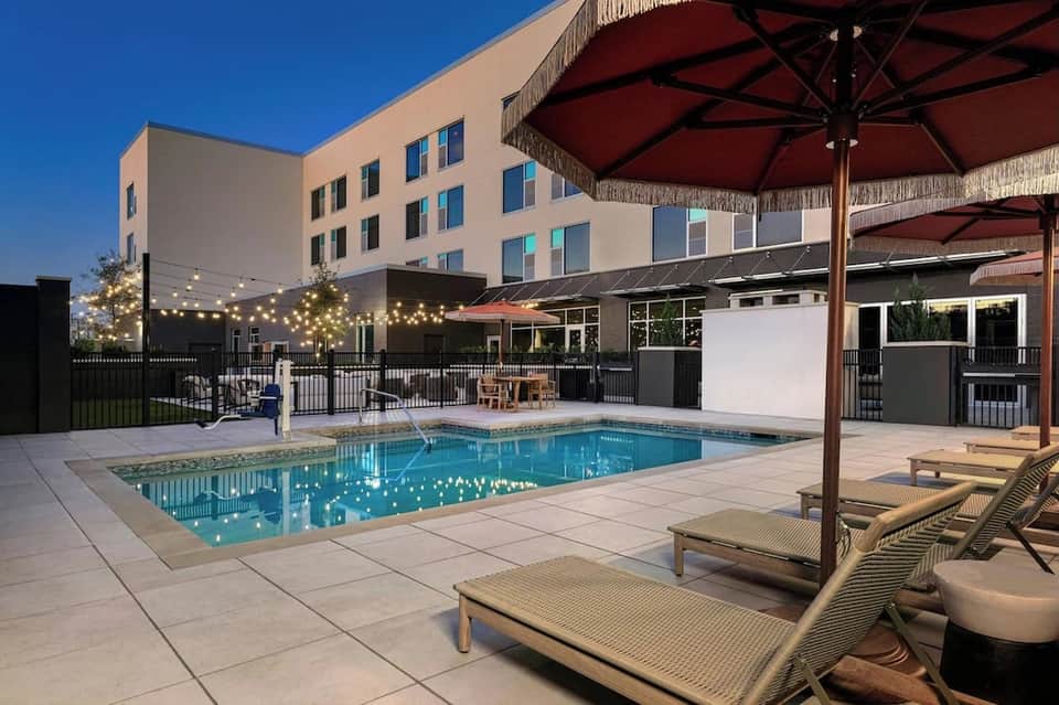 Evening pool area with lounge chairs, red umbrellas, and string lights