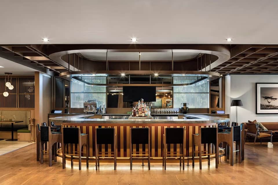 Modern hotel bar with curved wooden counter, glass panels, and contemporary lighting