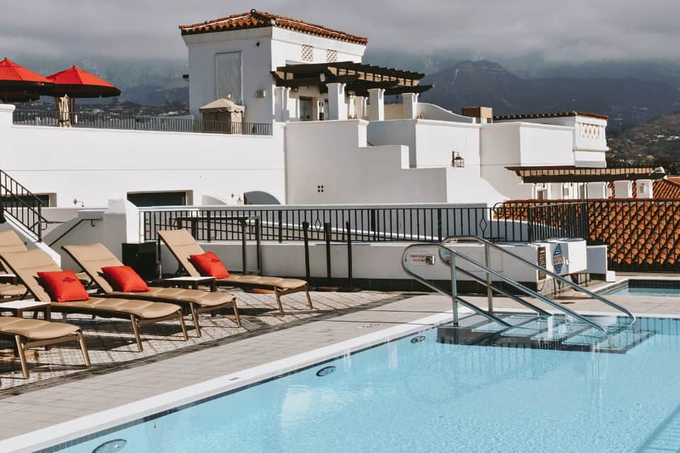 Hilltop resort pool with mountain views, lounge chairs with red cushions, and white architecture