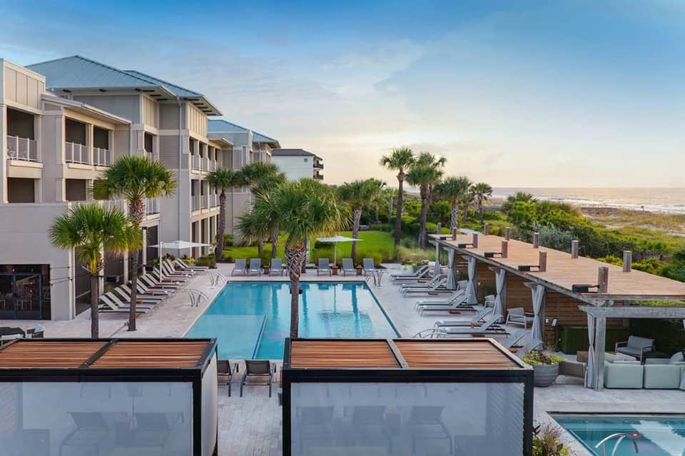 Beachfront resort pool with oceanview, palm trees, lounge chairs, and white buildings