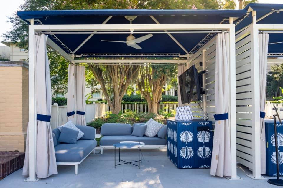 Outdoor pergola with white frame, navy curtains, ceiling fan, and blue cushioned seating