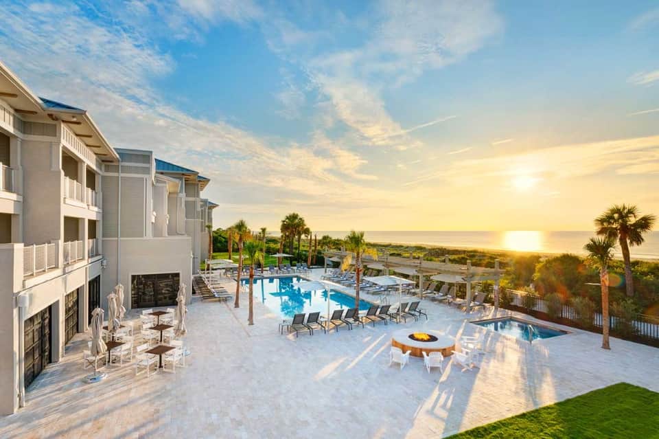 Oceanfront resort at sunset with pool, palm trees, fire pit, and coastal landscape views