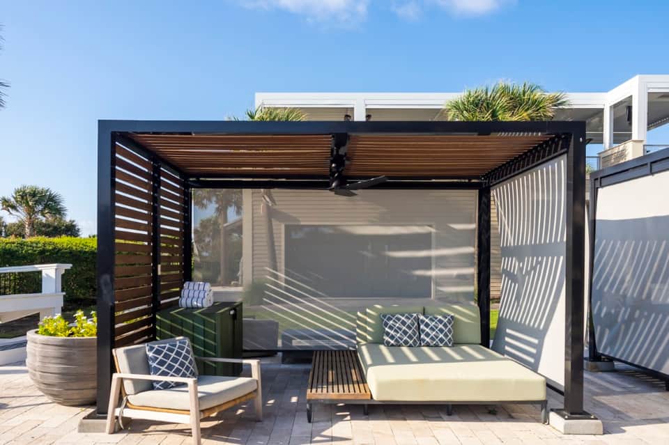Modern black pergola with retractable shade, cushioned seating, and louvered privacy panels on terrace