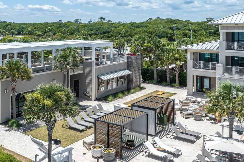 Aerial view of multi-level resort with rooftop lounge, palm trees, modern architecture, and natural preserve