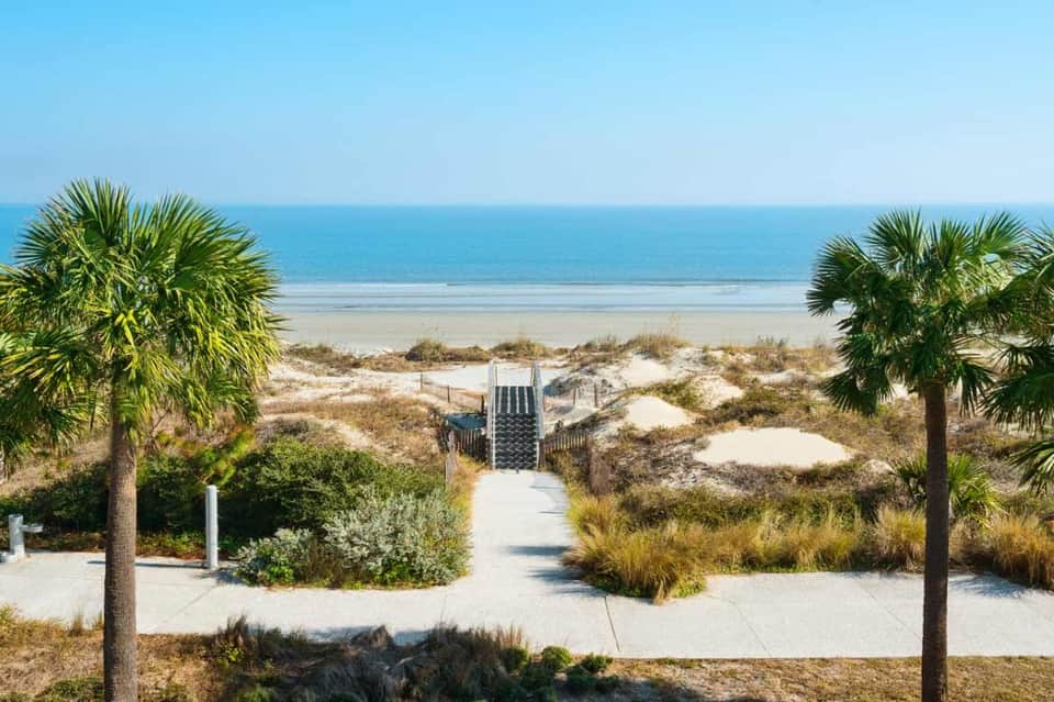 Beach access view with palm trees framing wooden boardwalk leading to sandy beach and turquoise ocean
