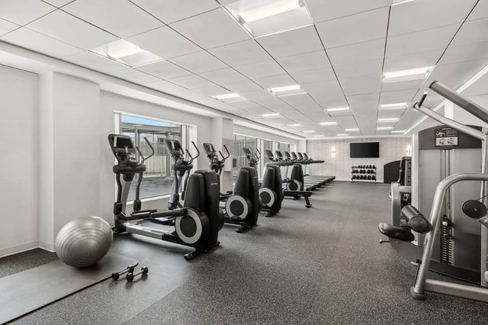Contemporary fitness center with cardio equipment, dumbbell rack, and access to outdoor patio