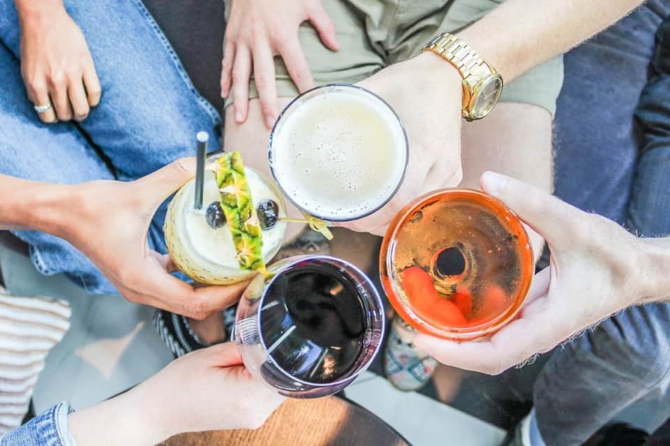 Group of people clinking glasses with colorful beverages and appetizers at outdoor social gathering