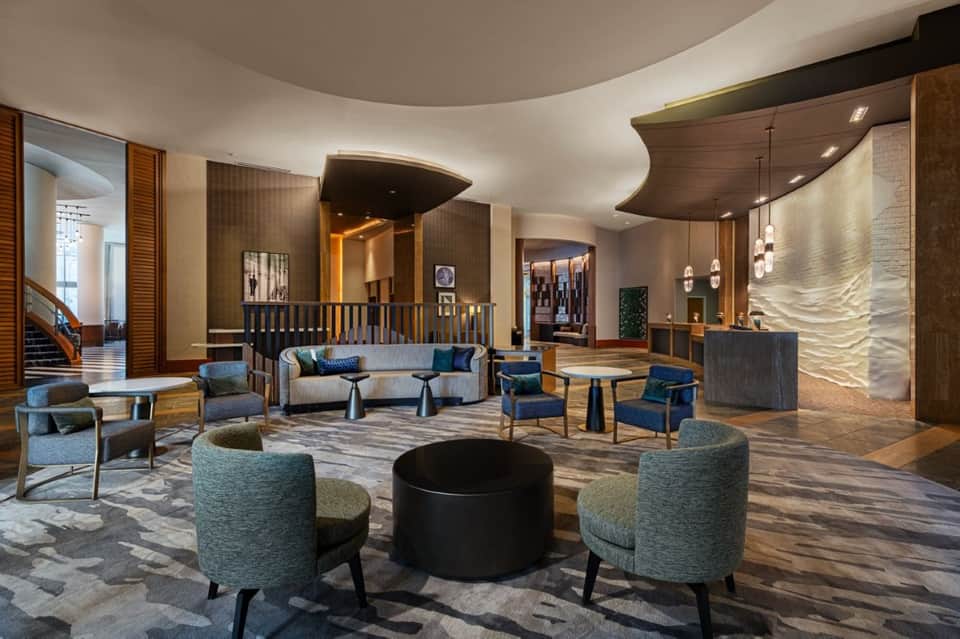 Elegant hotel lobby with curved architectural elements, teal accent chairs, fireplace, and modern furnishings