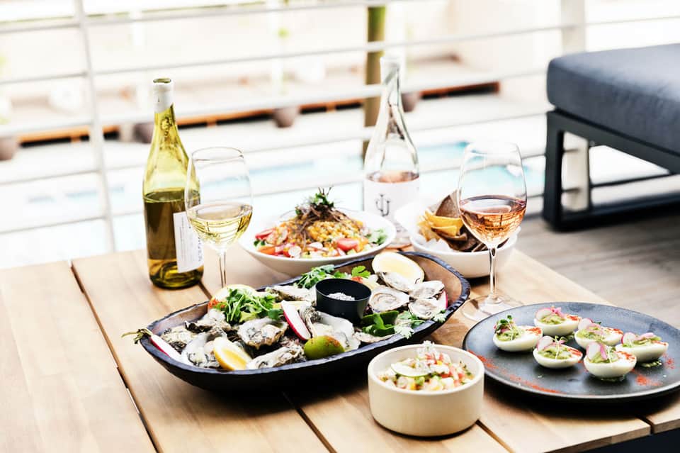 Elegant seafood dining spread with oysters, appetizers, white wine, and rosé wine on wooden table overlooking water