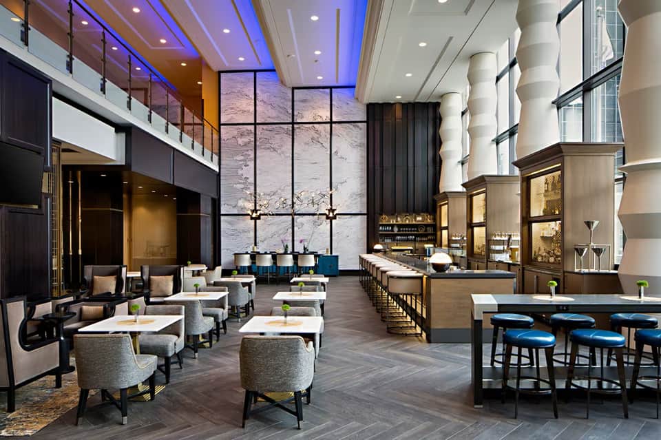 Spacious hotel lobby bar with modern columns, marble details, and dual-level seating areas
