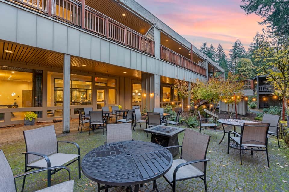 Modern resort patio at dusk with fire pit tables, lounge chairs, and illuminated building