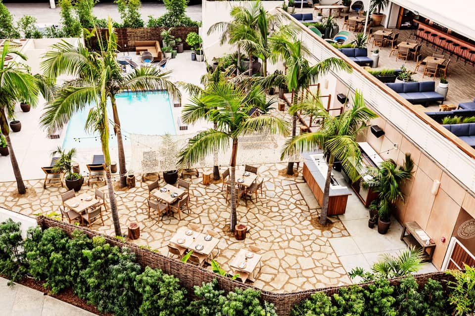 Aerial view of resort courtyard with pool, palm trees, lounge chairs, dining tables on stone patio