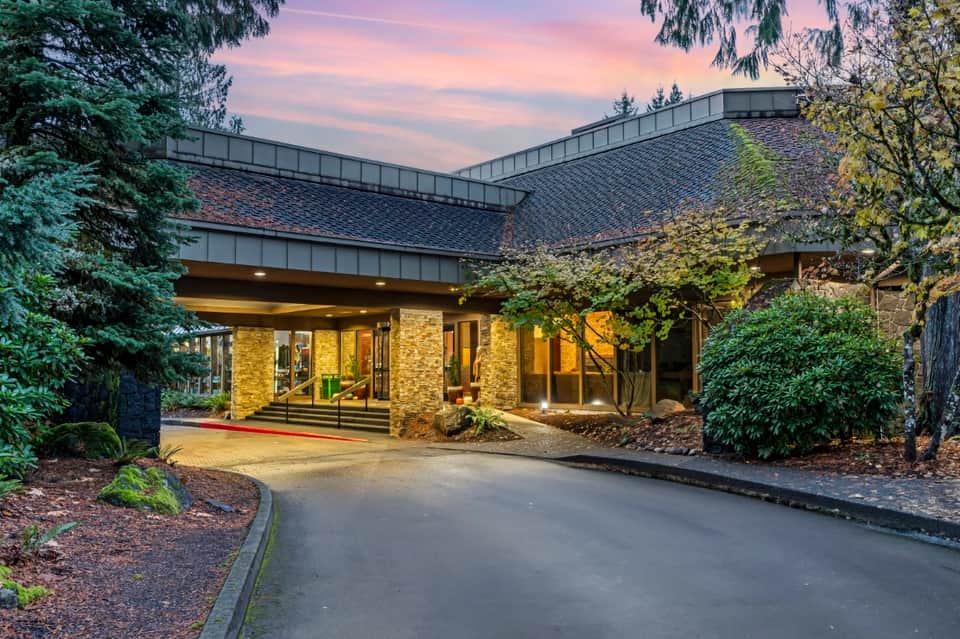 Modern lodge entrance at dusk with curved architecture, stone facade, and landscaping