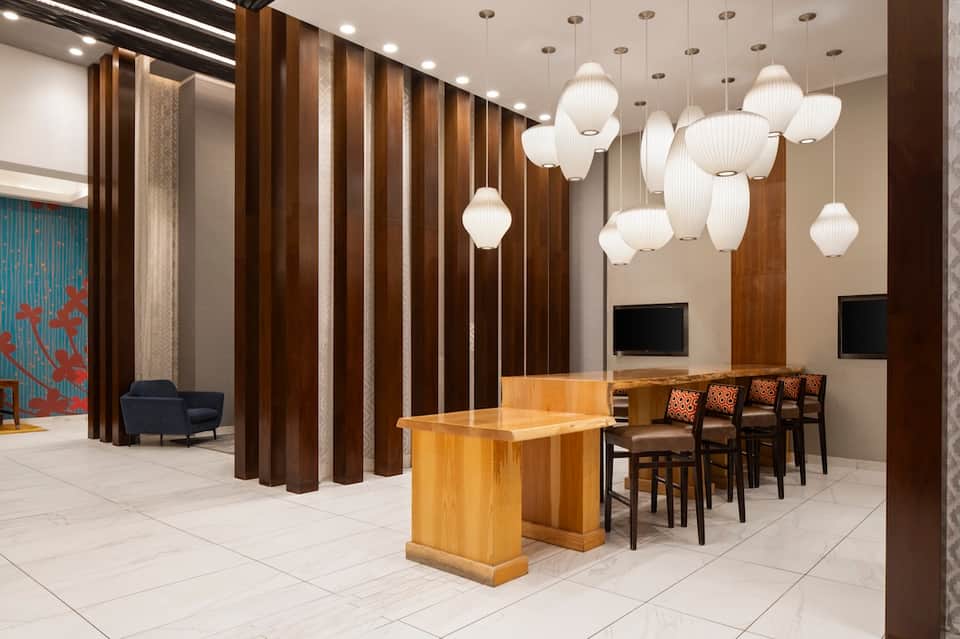 Modern hotel lobby with wood accent walls, elegant pendant lights, seating area, and contemporary design