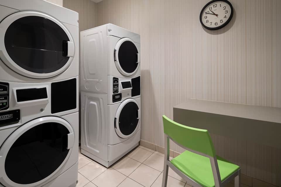 Hotel laundry facility with stacked washers and dryers, folding table, and wall clock